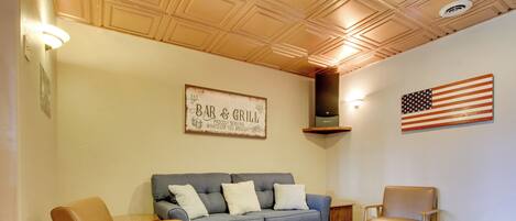 A living room with a sofa, two armchairs, a coffee table, and a rug. There is a sign on the wall that reads "BAR & GRILL" and an American flag.