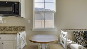 Uma cozinha com micro-ondas, janela com vista para uma cerca, mesa redonda de madeira com duas cadeiras e um sofá com almofada estampada.