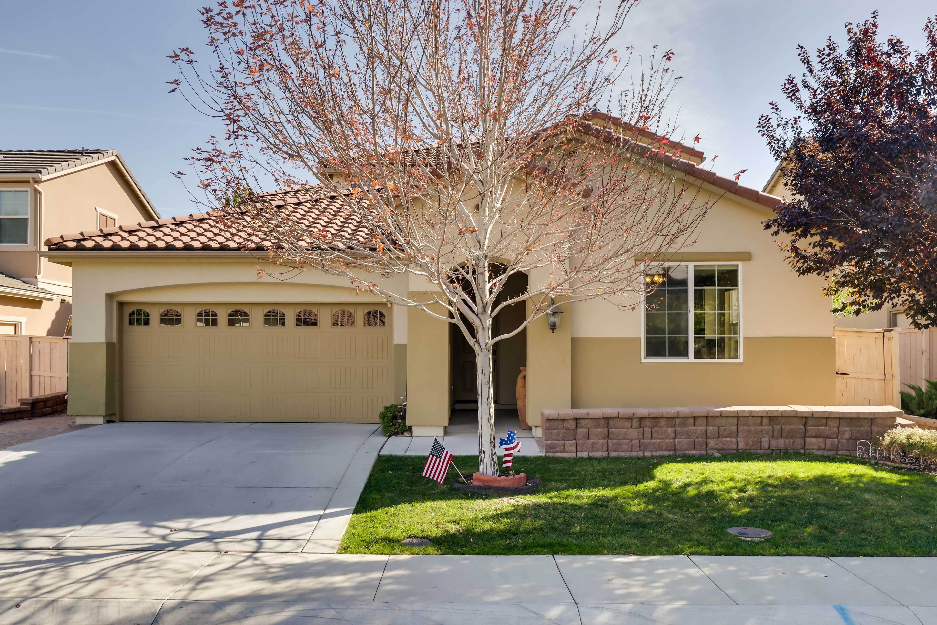 A single-story house with a garage, a tree in front, and an American flag on the lawn.