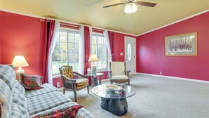 A living room with red walls, a plaid sofa, a glass coffee table, and a ceiling fan. - Spacious De Tour Village Home Near Lake Huron! (De Tour Village)