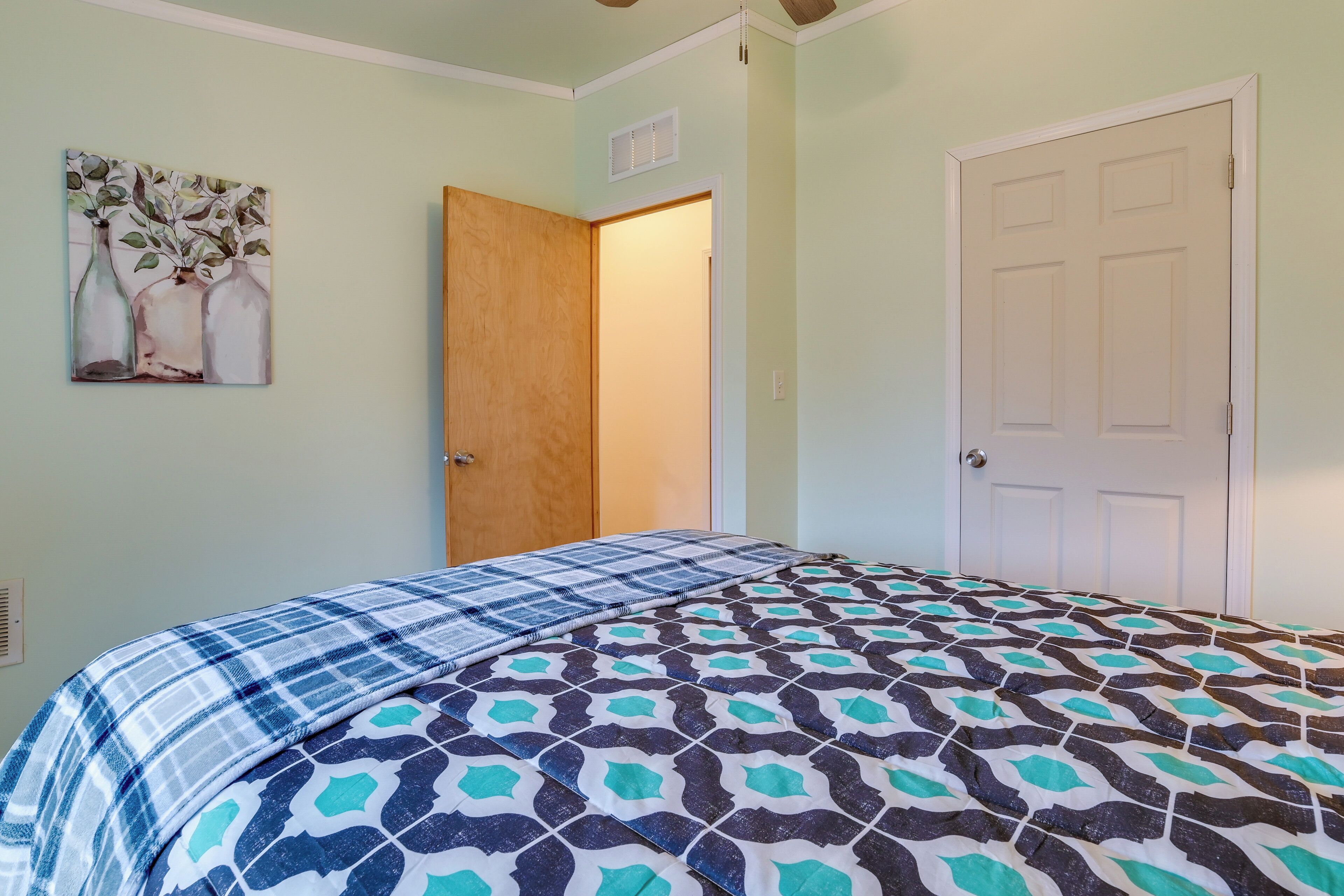 A bedroom with a bed, a door, and a wall-mounted painting.