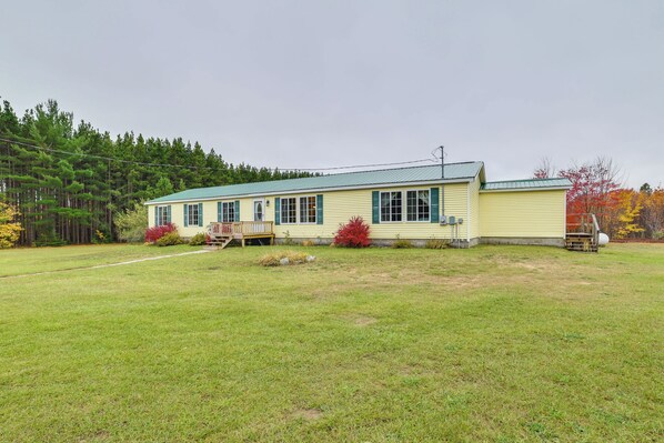A single-story yellow building with a green roof, a porch, and a small garden area with red bushes. - Spacious De Tour Village Home Near Lake Huron! (De Tour Village)