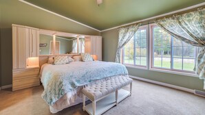 A bedroom with a bed, a bench, a ceiling fan, and large windows with curtains. - Spacious De Tour Village Home Near Lake Huron! (De Tour Village)