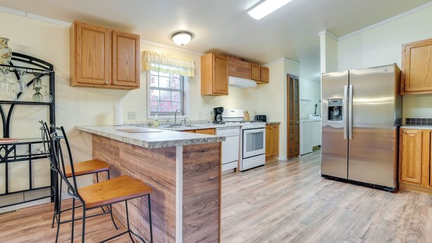 A kitchen with wooden cabinets, a stainless steel refrigerator, a coffee maker, and a window with a curtain. - Spacious De Tour Village Home Near Lake Huron! (De Tour Village)