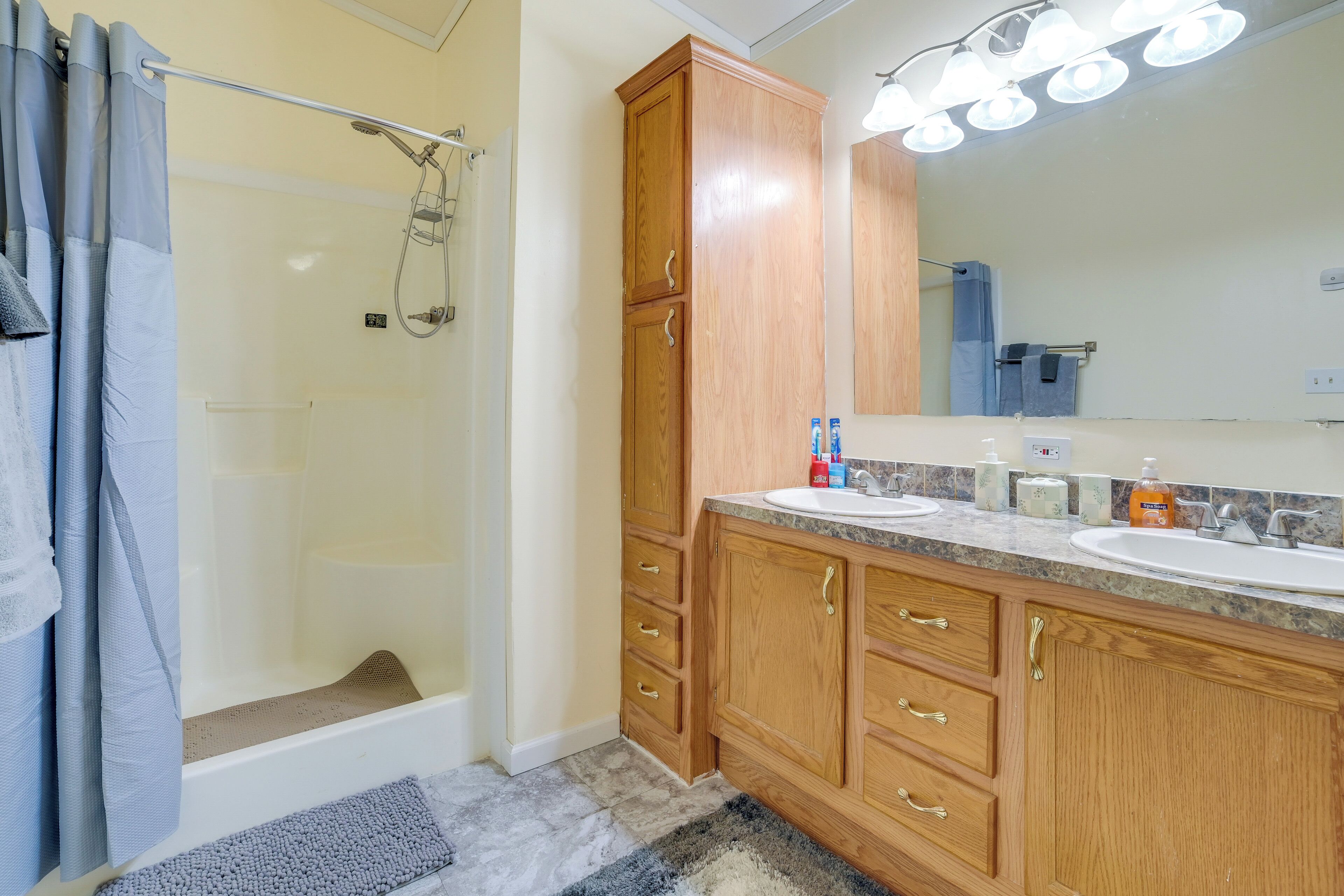 A bathroom with a shower, two sinks, wooden cabinets, and a large mirror.