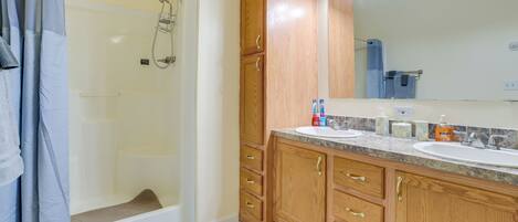 A bathroom with a shower, two sinks, wooden cabinets, and a large mirror.