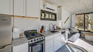 Ett modernt kök med vita skåp, en inbyggd spis och ett stort fönster med utsikt över träd.