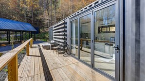 En modern stuga med en veranda, stora skjutbara glasdörrar och utsikt över den omgivande skogen.
