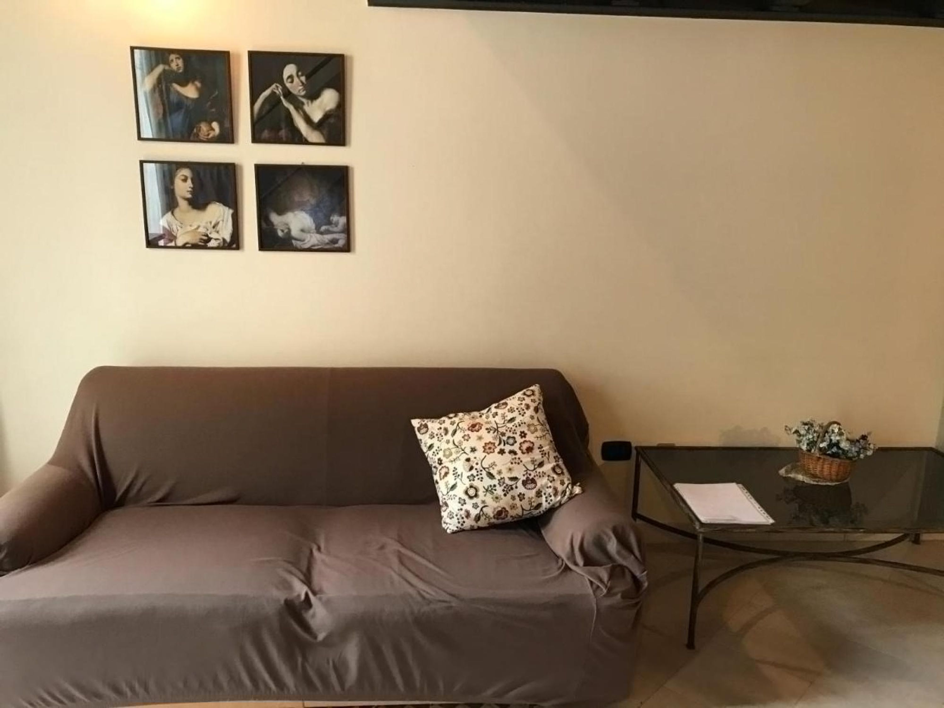 A living room with a brown sofa, a floral pillow, and four framed artworks on the wall.