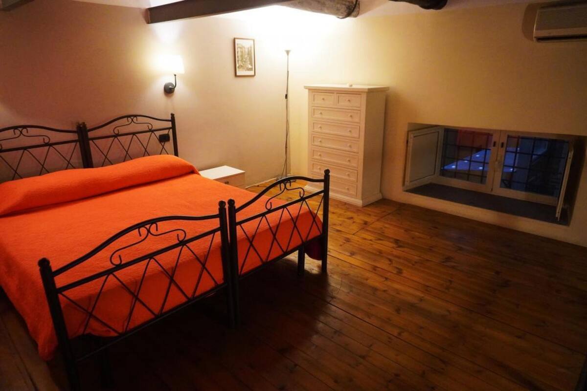 Ein Schlafzimmer mit Holzboden, einem Bett mit orangefarbener Bettdecke, einem weißen Schminktisch und einem Fenster mit Blick.
