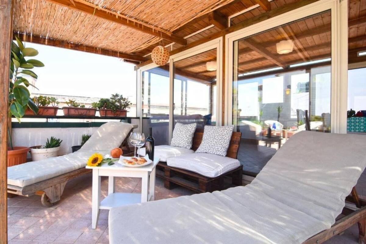 Ein sonniger Außenbereich mit Lounge-Möbeln und einem Tisch, umgeben von Topfpflanzen und Blick auf die Stadt.