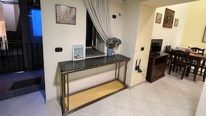 Une chambre d’hôtel avec une console en verre, une petite plante, un panneau indiquant « VISITE », un téléviseur et un coin repas avec des chaises et une table.