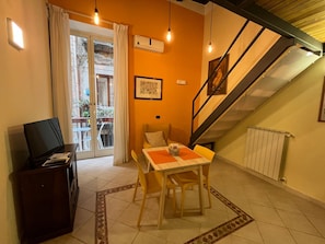 A dining area with a table and chairs, a television on a cabinet, and a staircase. - Case Cosi Napoli (Naples)