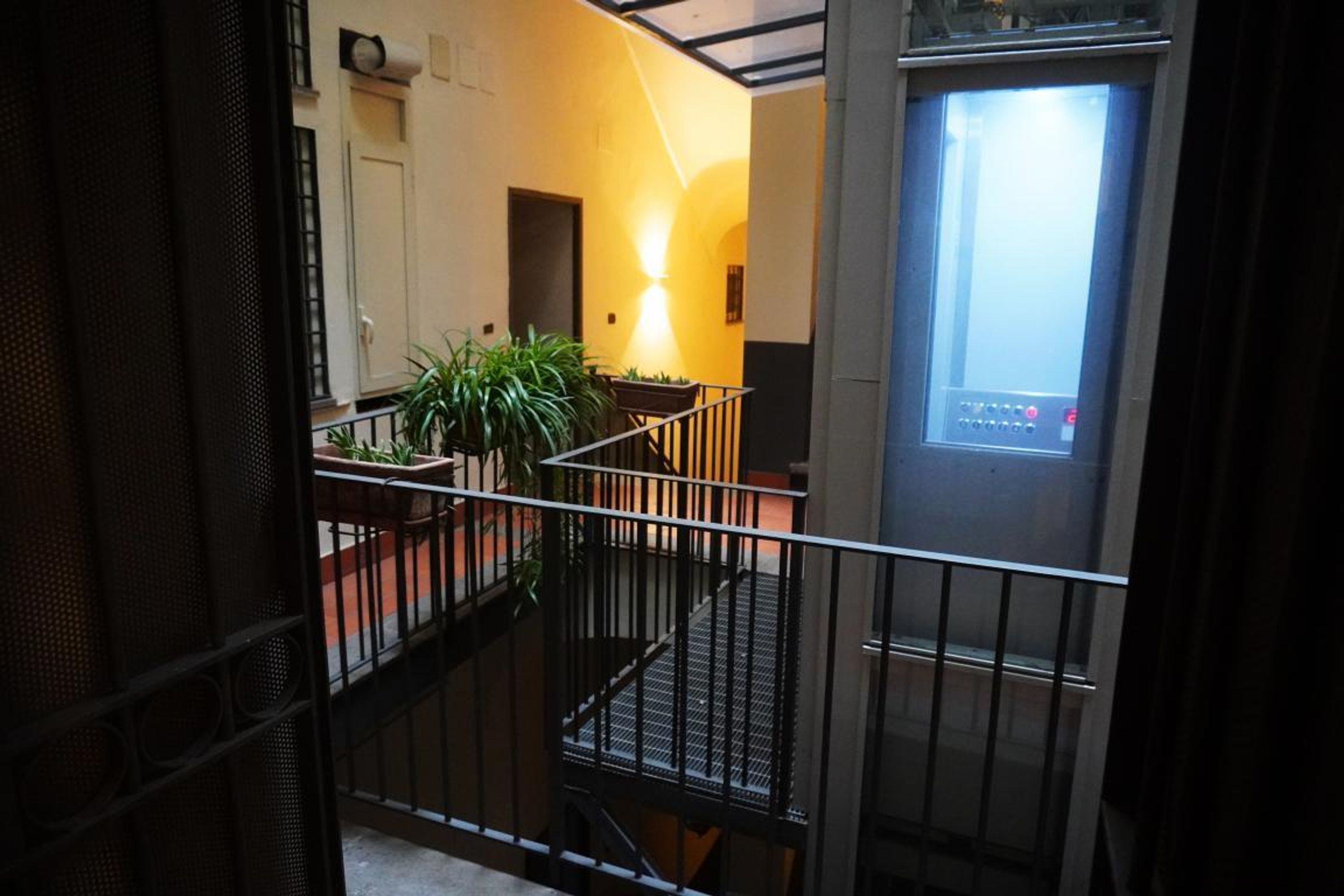Una escalera con barandilla de metal, una planta en maceta y una lámpara fijada a la pared.