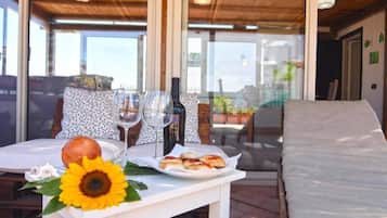 An outdoor dining area with a table set for two, featuring a plate of food, a bottle of wine, and a sunflower decoration.