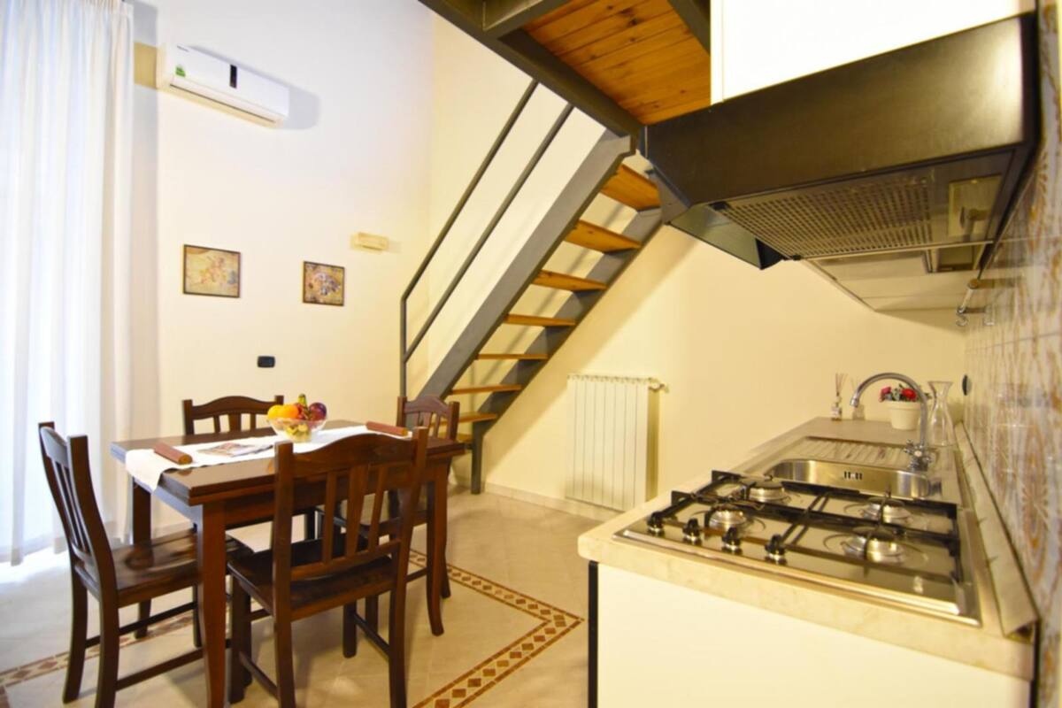 Eine kleine Küche mit Gaskochfeld, Holzkohlenstühlen, einem Esstisch und einer Treppe, die in ein Obergeschoss führt.