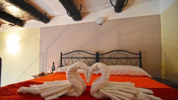 Une chambre d’hôtel avec un lit, une couverture rouge et des serviettes disposées en forme de cœur.