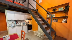 Une cuisine de taille réduite avec des meubles blancs, une chaise rouge et un escalier menant à un niveau inférieur.