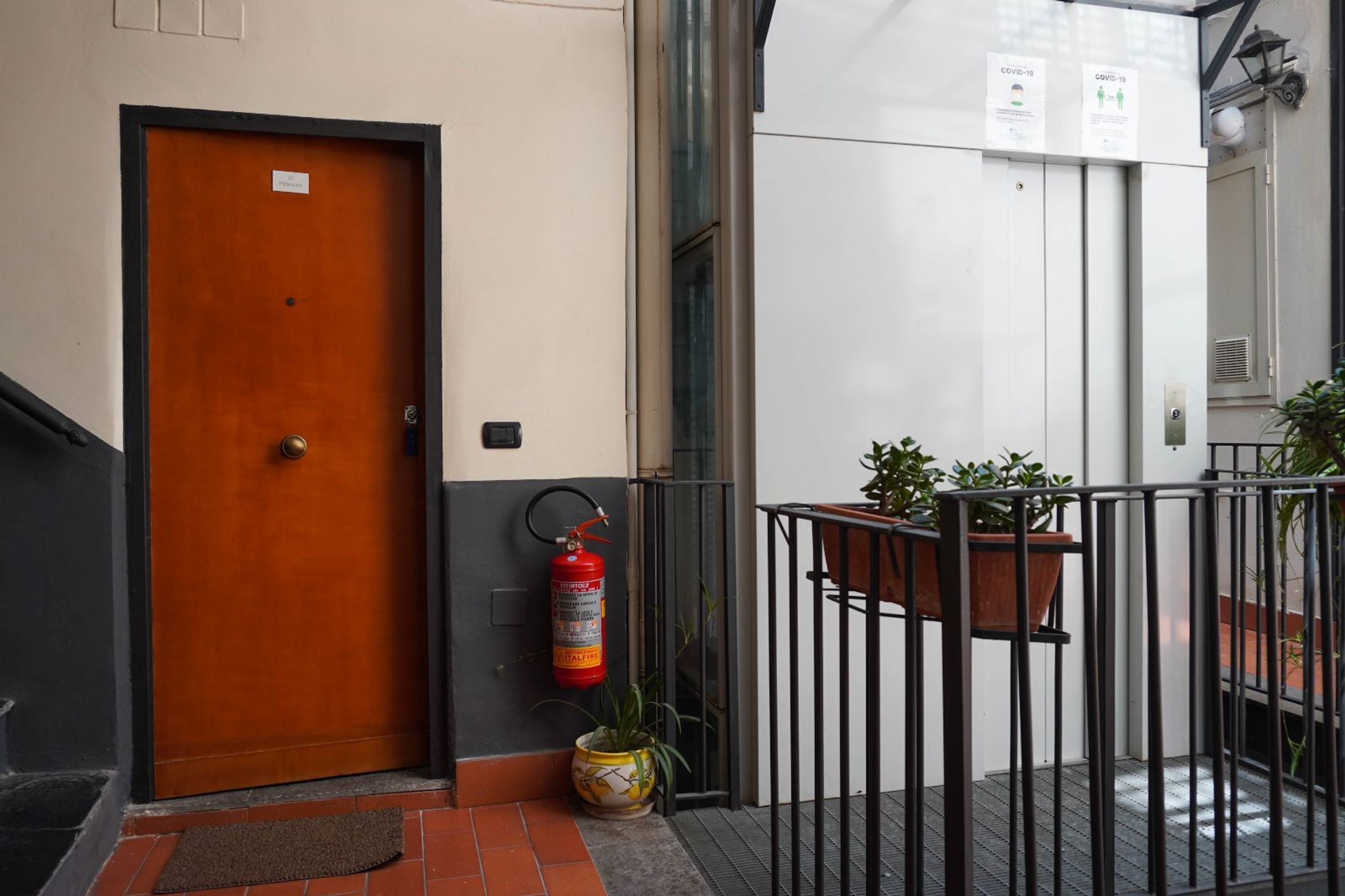 Ein Hotel Eingang mit einer Holztür, einem Feuerlöscher und Topfpflanzen.