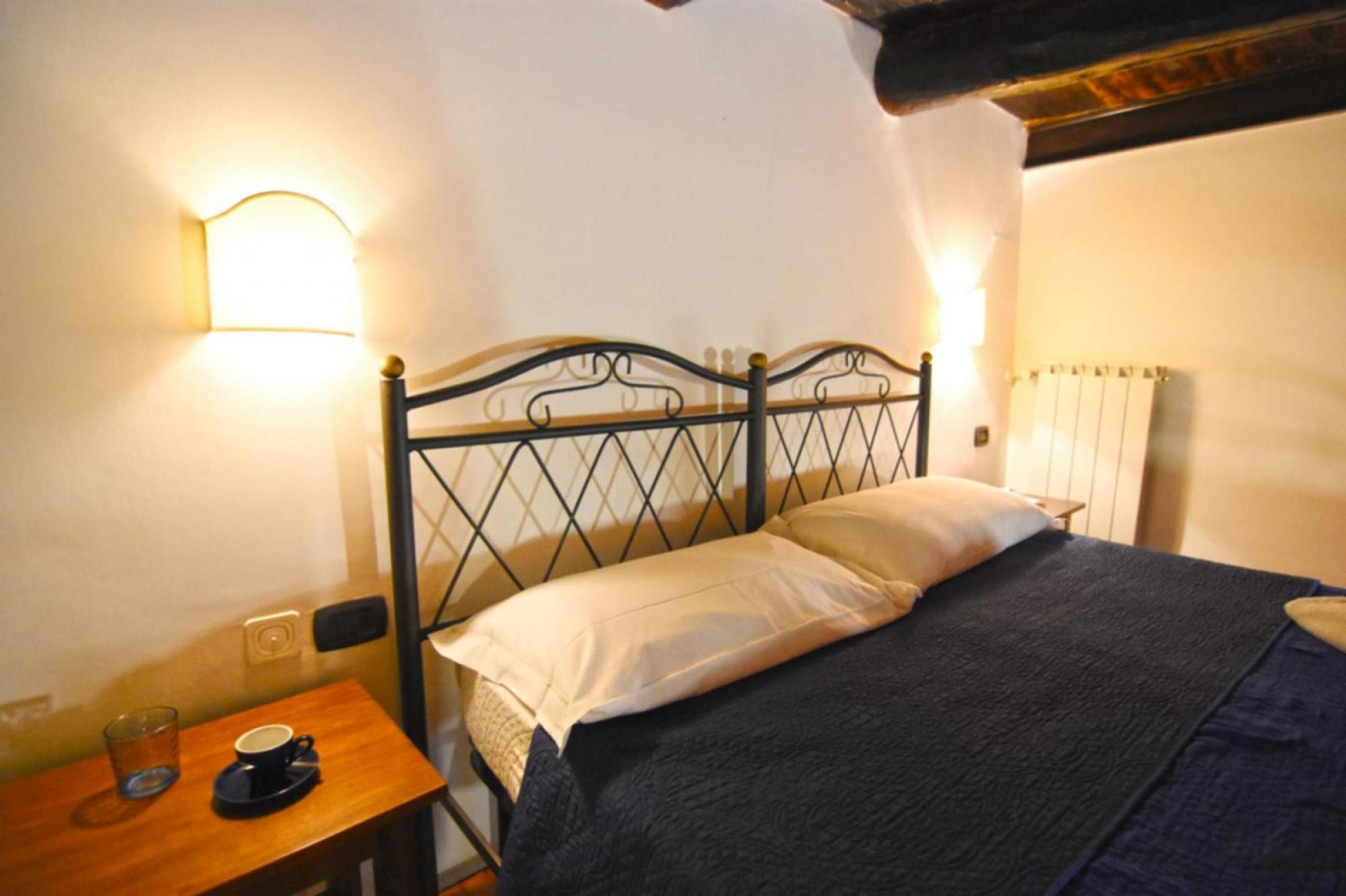 A room with a bed, a nightstand, a cup and saucer, and a wall-mounted light fixture.