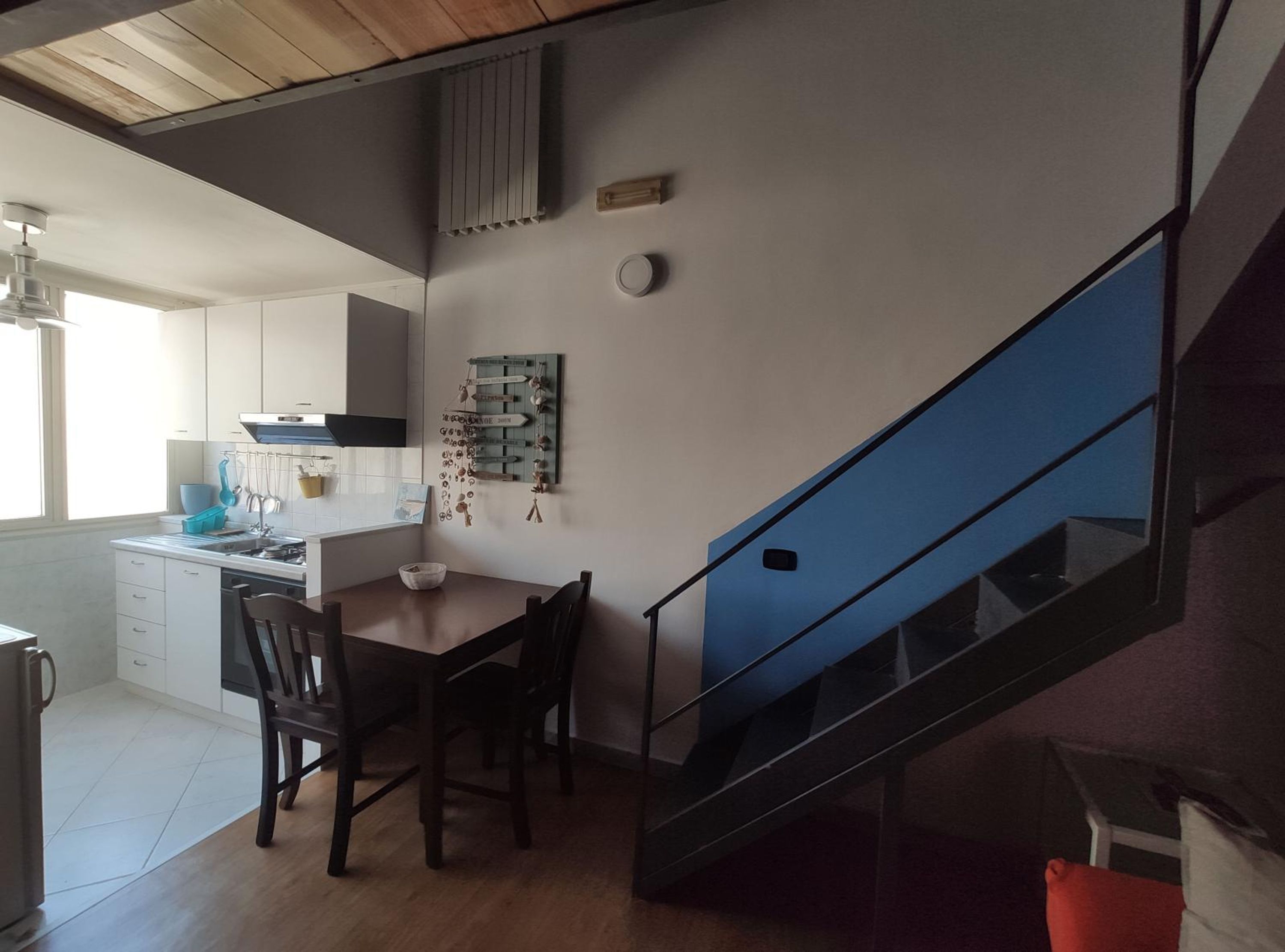 Eine Küche mit weißen Schränken, einem Holzespeise Tisch und einer blauen Treppe.
