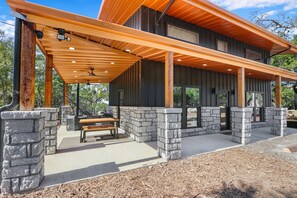 Un espace extérieur abrité, doté d’un banc en pierre et d’un barbecue, de poutres en bois et offrant une vue sur le paysage environnant.