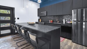 Una cocina moderna con una isla central, armarios oscuros, electrodomésticos de acero inoxidable e iluminación colgante.