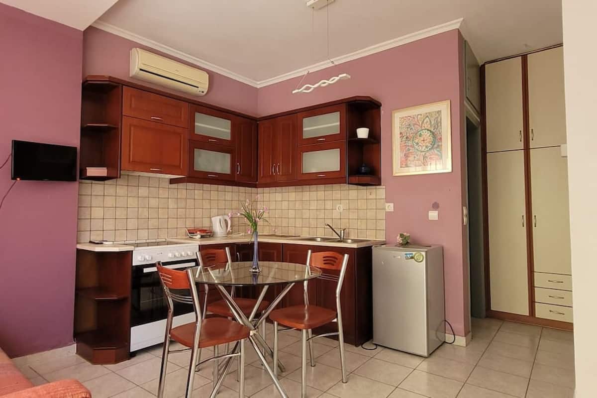 A compact kitchen with wooden cabinets, a built-in oven, a refrigerator, and a dining table with chairs.
