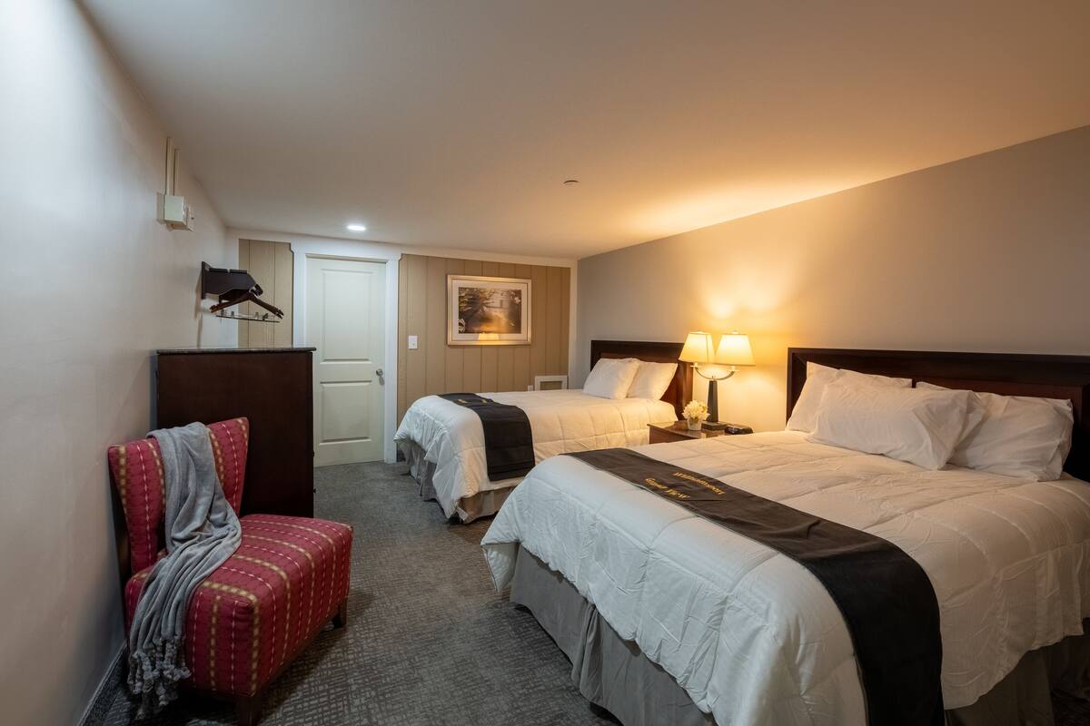 A hotel room with two beds, a desk, a chair, and a door.