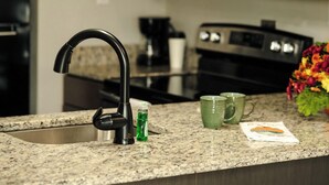 A kitchen with a modern faucet, granite countertop, and a coffee maker. - Lock Haven Grandview Hotel (Mill Hall)