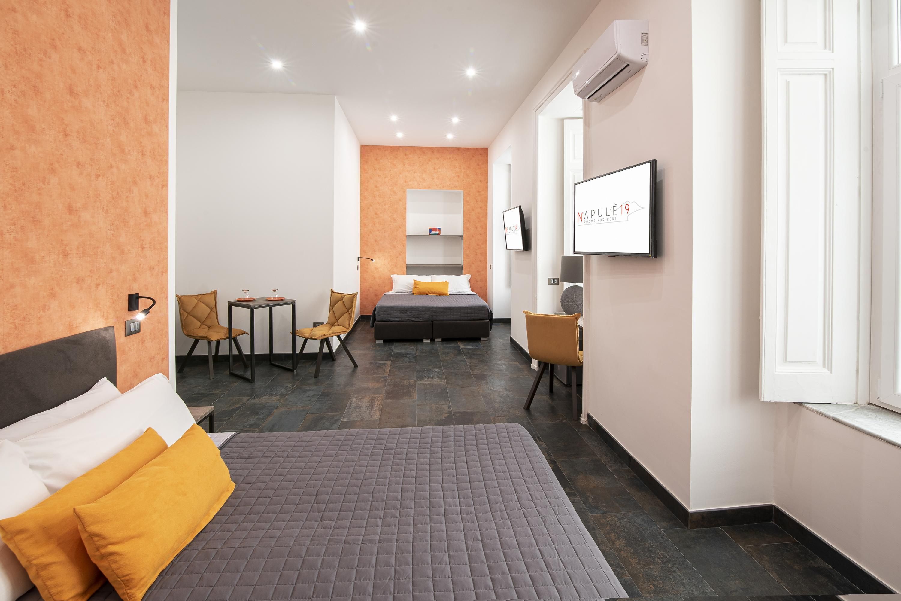 A hotel room with a bed, a desk, a chair, a TV, and a wall-mounted air conditioner.