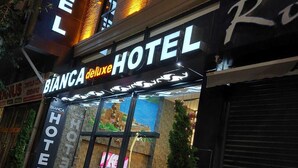 Entrada de hotel com uma placa indicando "BIANCA deluxe HOTEL" e o logotipo visível.