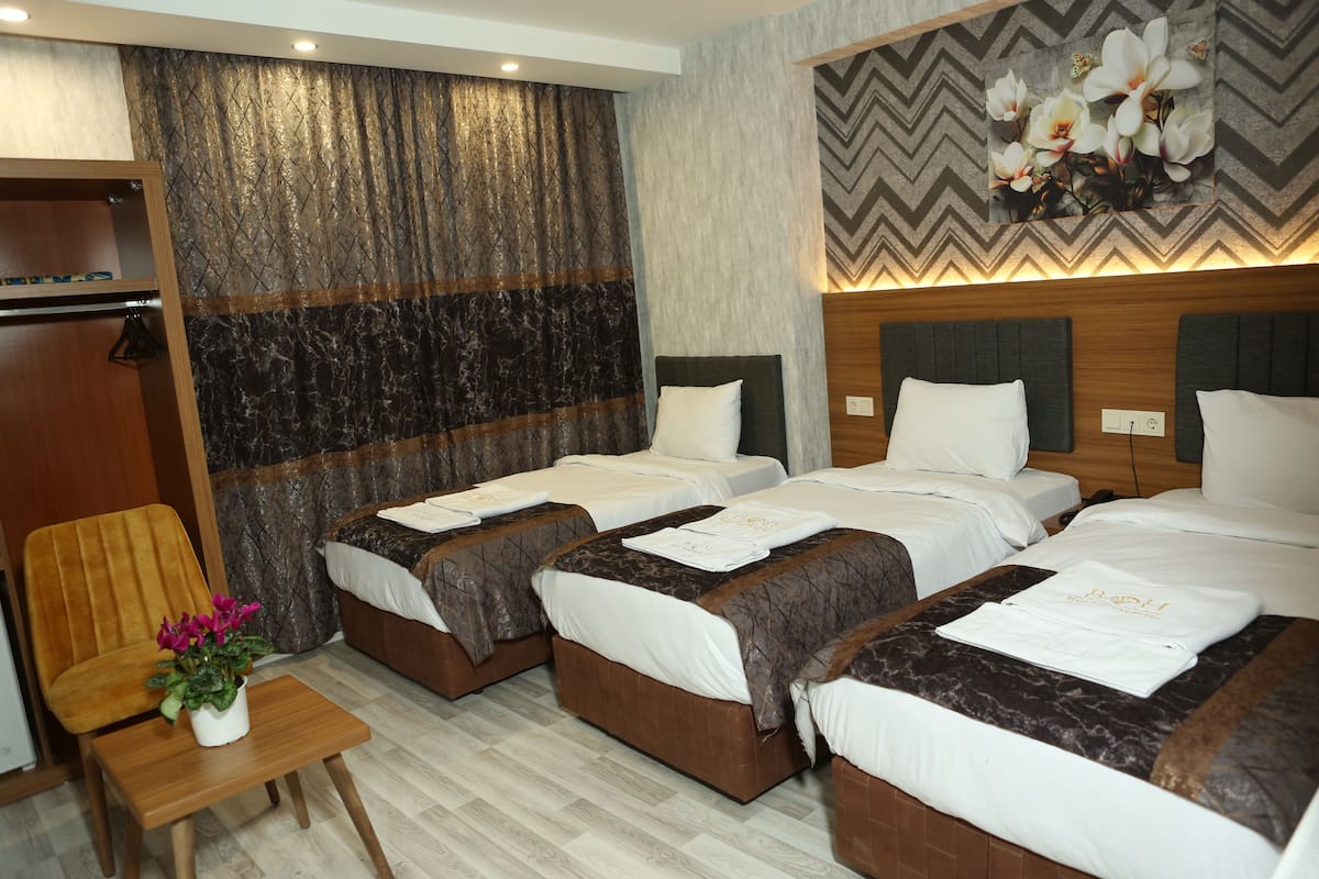 A hotel room with three beds, a wooden chair, a small table with a potted plant, and a decorative wall with a chevron pattern.