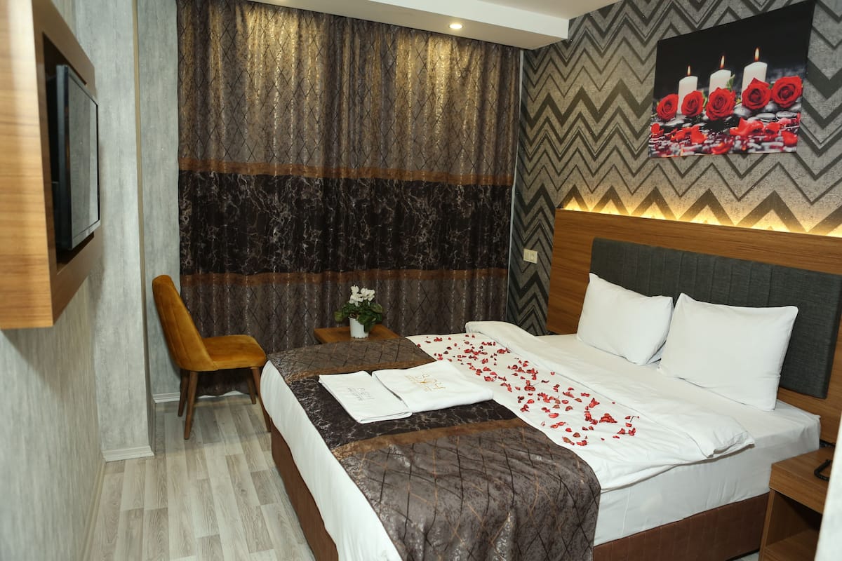 A hotel room with a bed, a desk, and a chair. There is a painting on the wall and a television mounted on the wall.