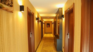 Um corredor de hotel com portas de madeira, luminárias fixadas na parede e piso coberto por carpete.