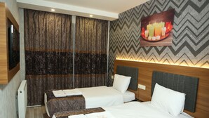 Quarto de hotel com duas camas, um espelho grande, uma televisão fixada na parede e um painel decorativo.
