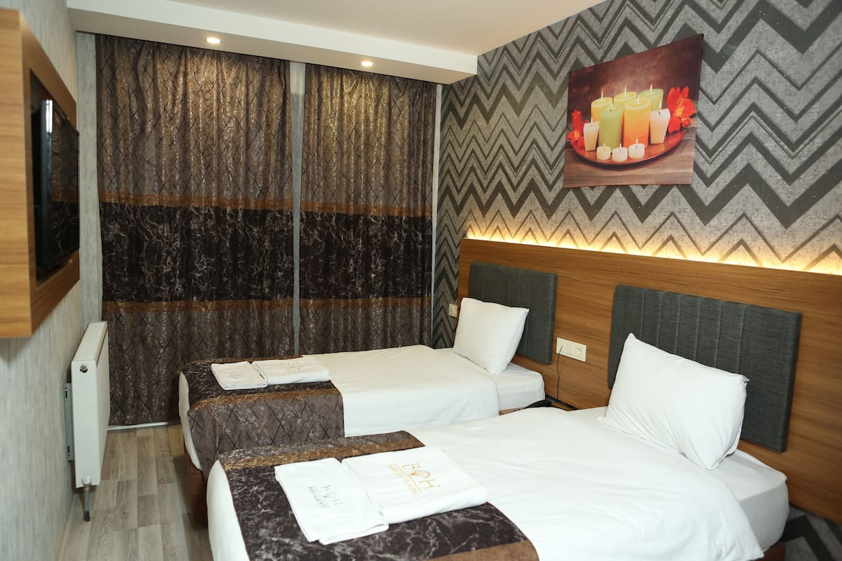 A hotel room with two beds, a large mirror, a wall-mounted TV, and a decorative wall panel.