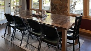 Uma área de refeições com uma grande mesa de madeira, cadeiras pretas e uma parede de pedra decorativa.