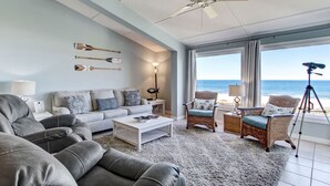 A living room with a sofa, armchairs, a coffee table, and a view of the ocean.