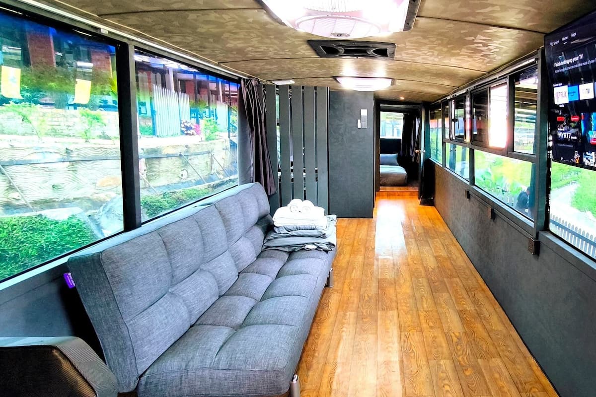 A train car with a wooden floor, grey upholstered seating, and a large screen displaying various content.