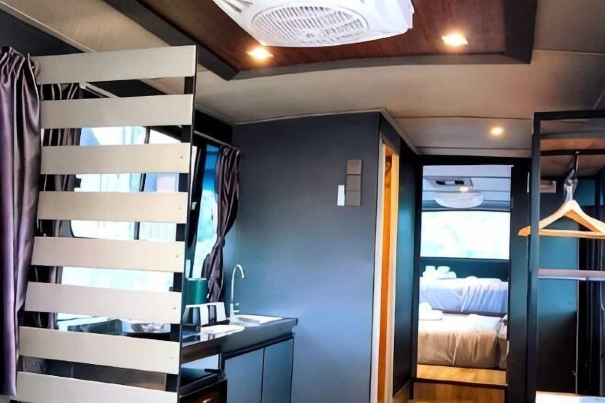 A room with a bed, a desk, a hanging light fixture, and a view of the outside.