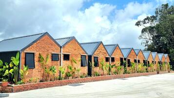 A row of brick buildings with triangular roofs, surrounded by greenery and a clear sky.