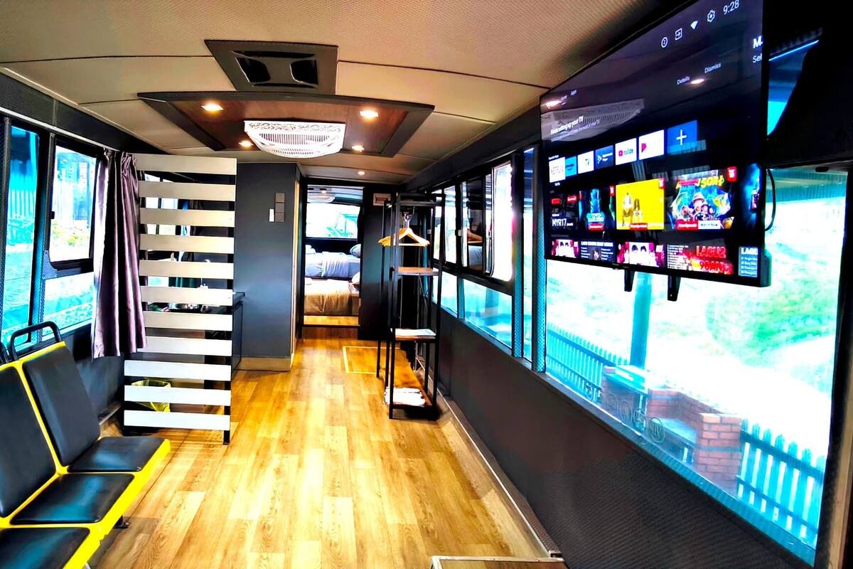A modern train interior with wooden flooring, black and yellow seating, a staircase, and large windows offering views of the outside.