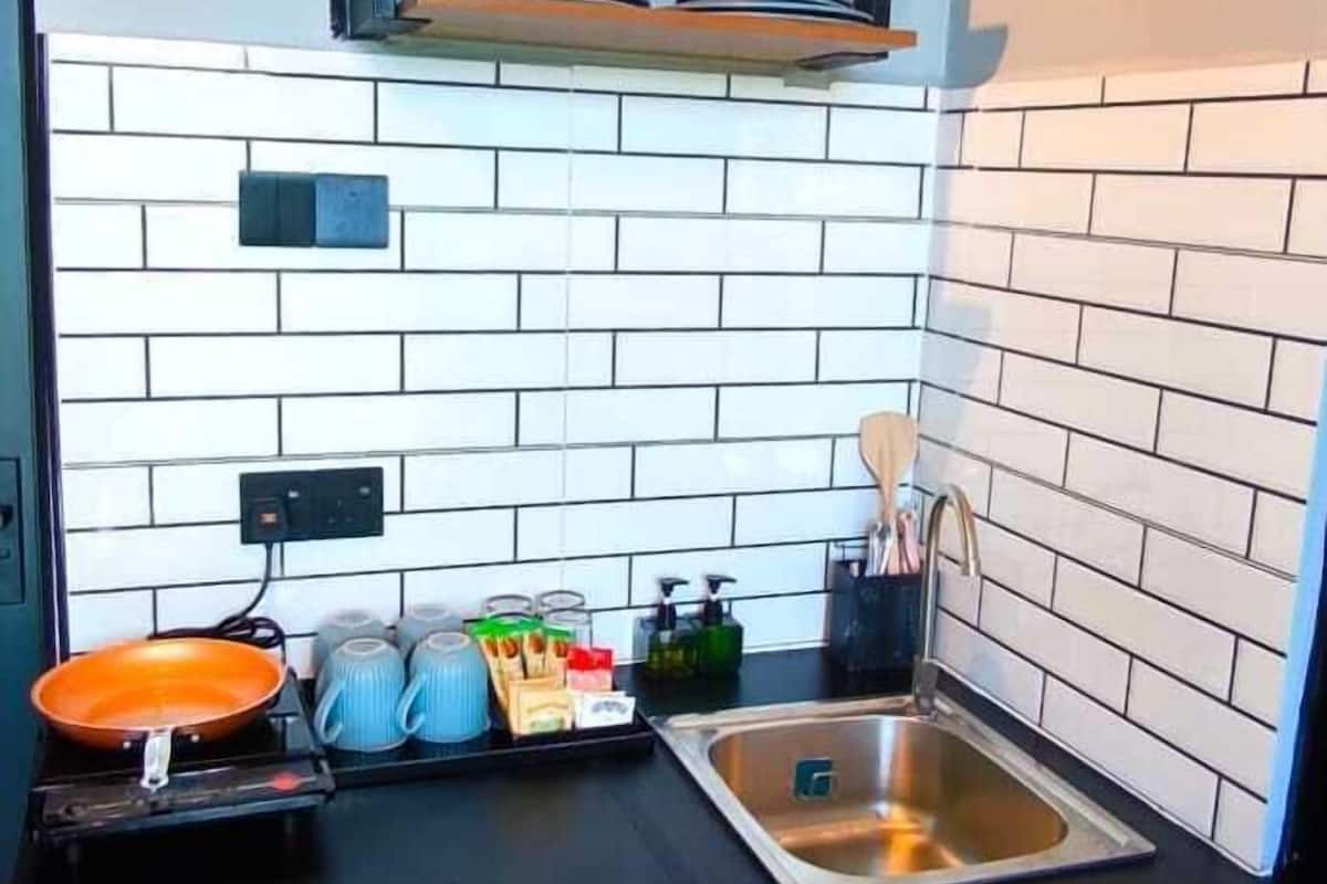A compact kitchen with a black countertop, wooden cabinets, a stainless steel sink, and a tiled backsplash.