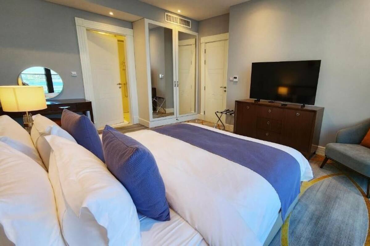 A hotel room with a large bed, a television, a chair, and a wardrobe.