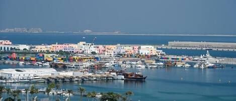 A coastal cityscape with colorful buildings, a marina with boats, and a distinctive white curved structure in the foreground.