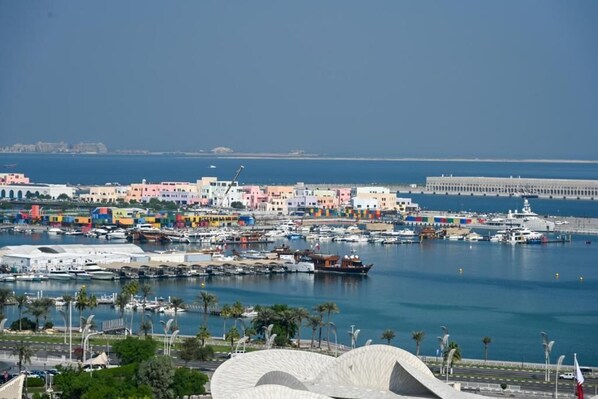 Un paisaje urbano costero con edificios coloridos, un puerto deportivo con barcos y una estructura blanca curva distintiva en primer plano.
