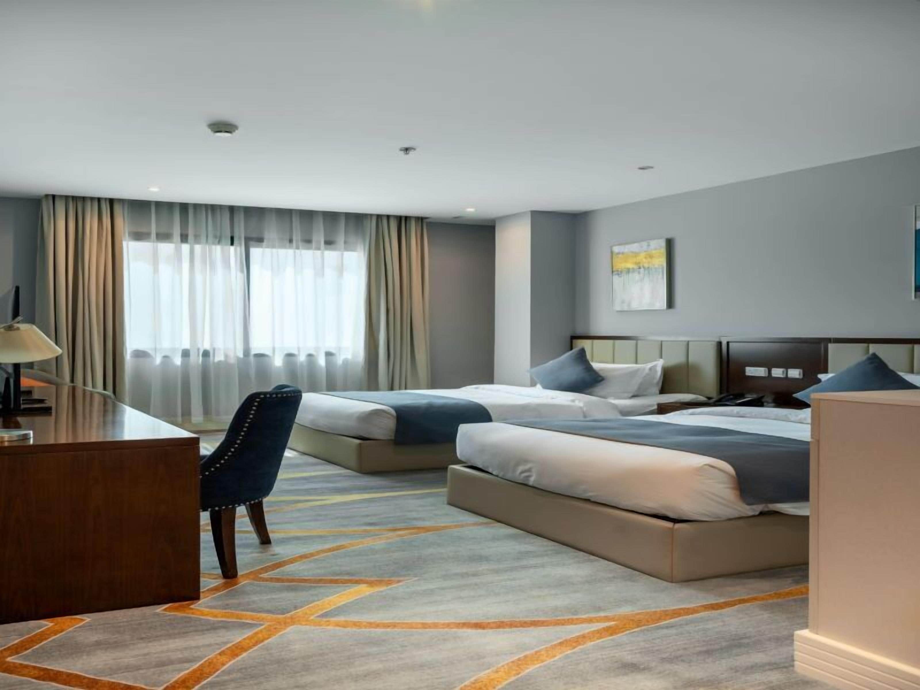 A hotel room with two beds, a desk, and a chair.