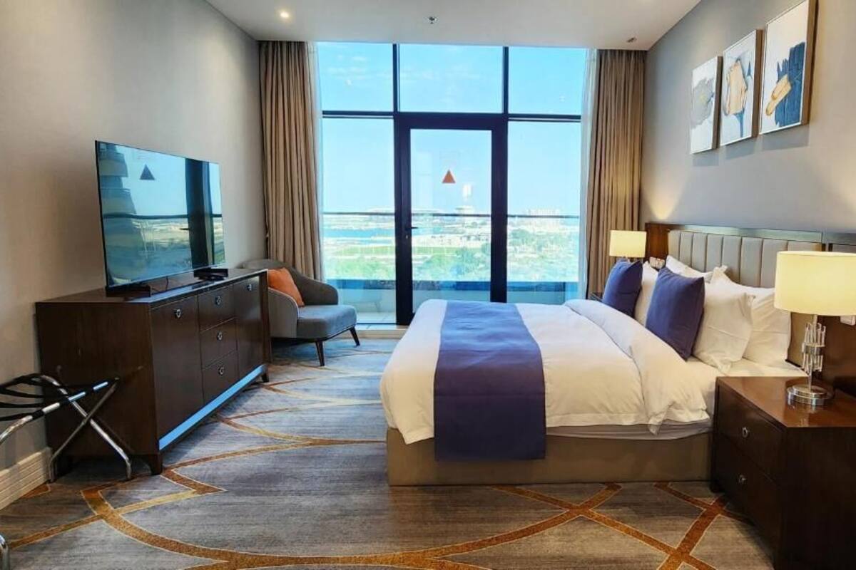 A hotel room with a large bed, a TV, a desk, and a view of the city.