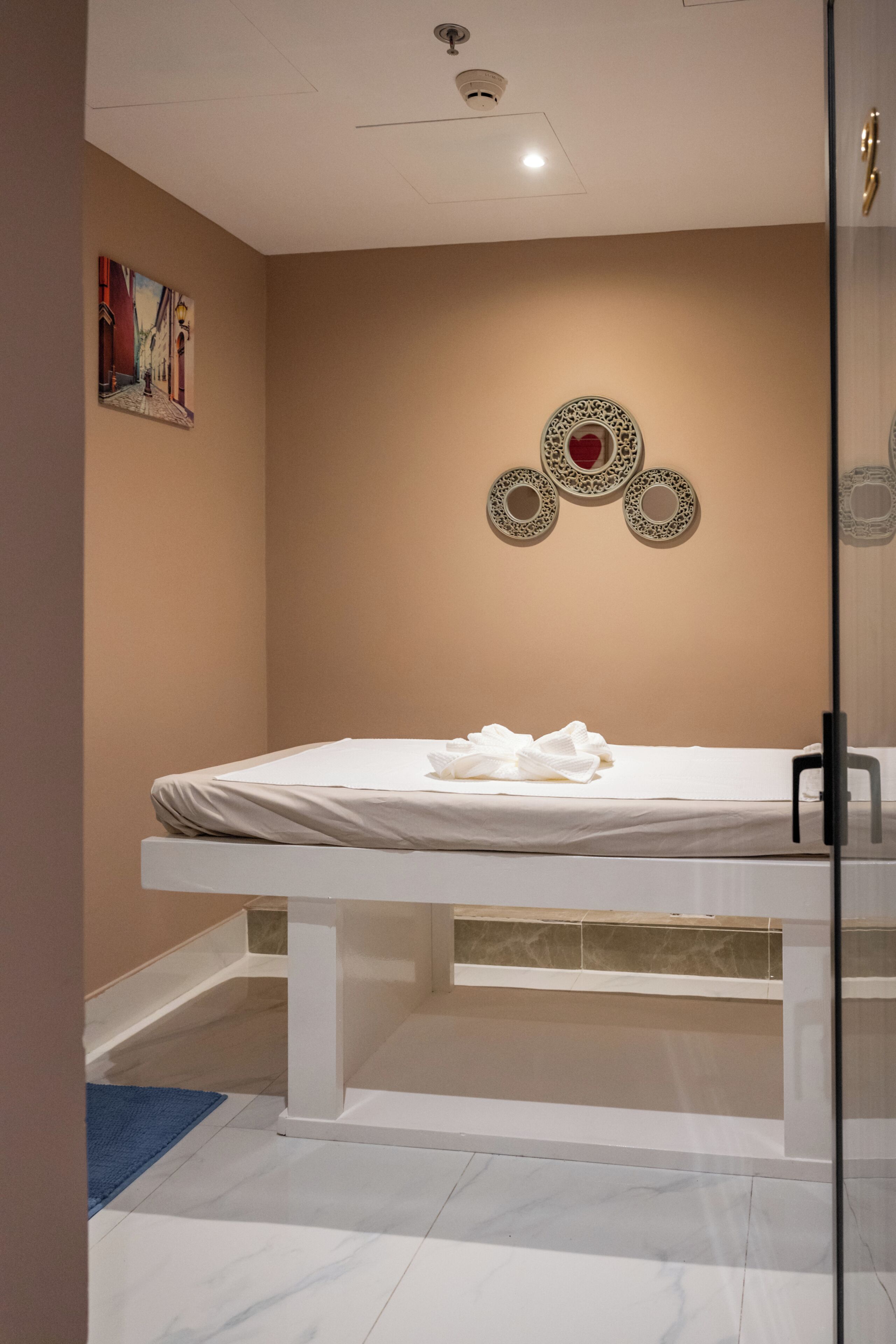 A room with a bed, a glass partition, a wall-mounted artwork, and a ceiling light.
